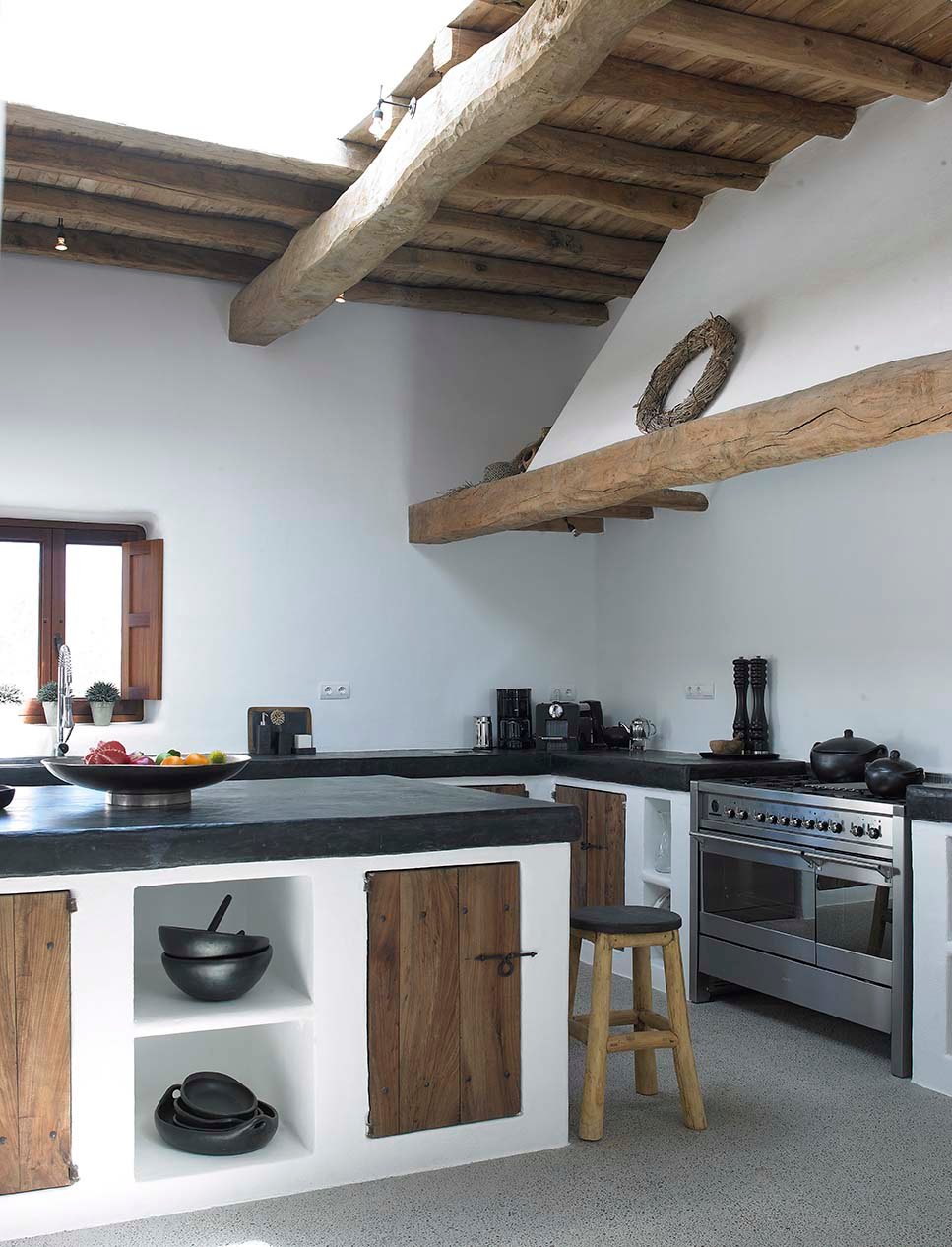 Bellissima cucina rustica con struttura muraria e isola centrale - colori bianco, nero e legno - pavimenti e top in cemento e soffitto con travi in legno