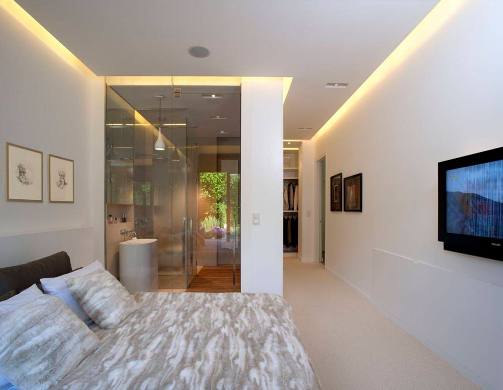 Moderna camera da letto con bagno interno realizzato con pareti in vetro. Il controsoffitto in cartongesso con luce a led che segue il perimetro della stanza.