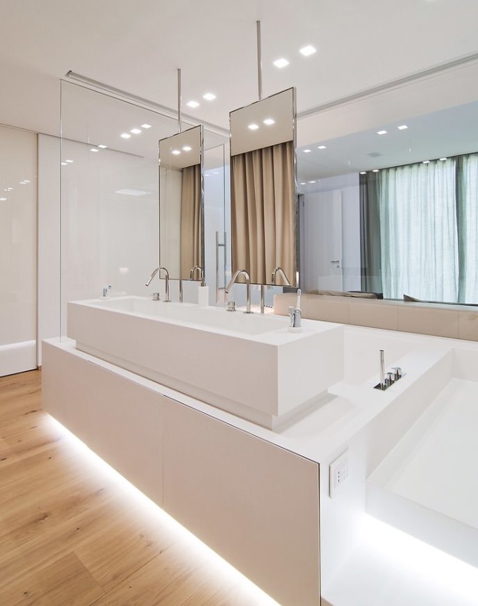 Bagno di design moderno con pareti bianche e pavimento in legno massello. La suddivisione dello spazio è realizzata con gli specchi sospesi. L’illuminazione artificiale gioca un ruolo fondamentale per creare l’atmosfera giusta per il massimo benessere e relax