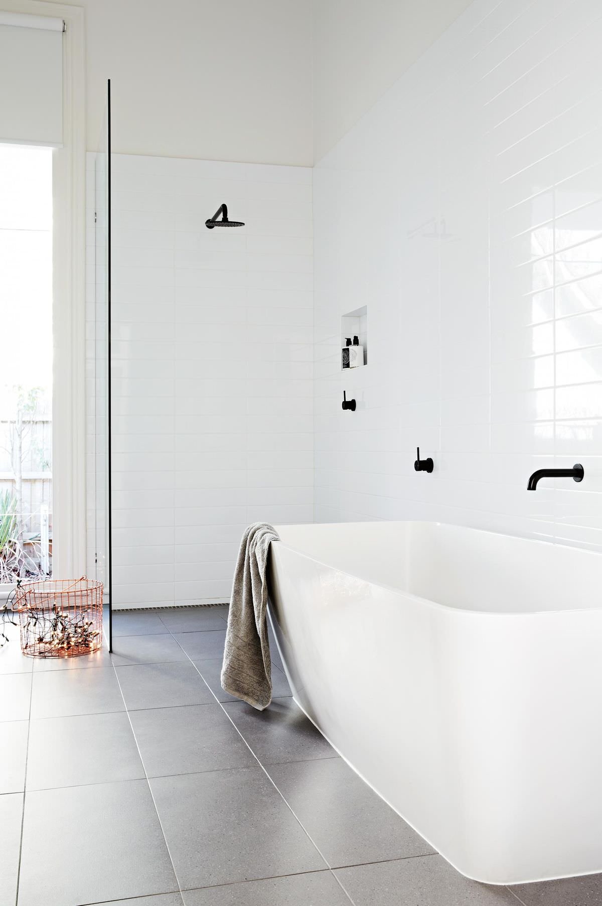 La scelta della rubinetteria nera conferisce a questo bagno bianco lucido un aspetto sottile ma dinamico. Il pavimento in piastrelle grigio aggiunge calore e profondità allo spazio
