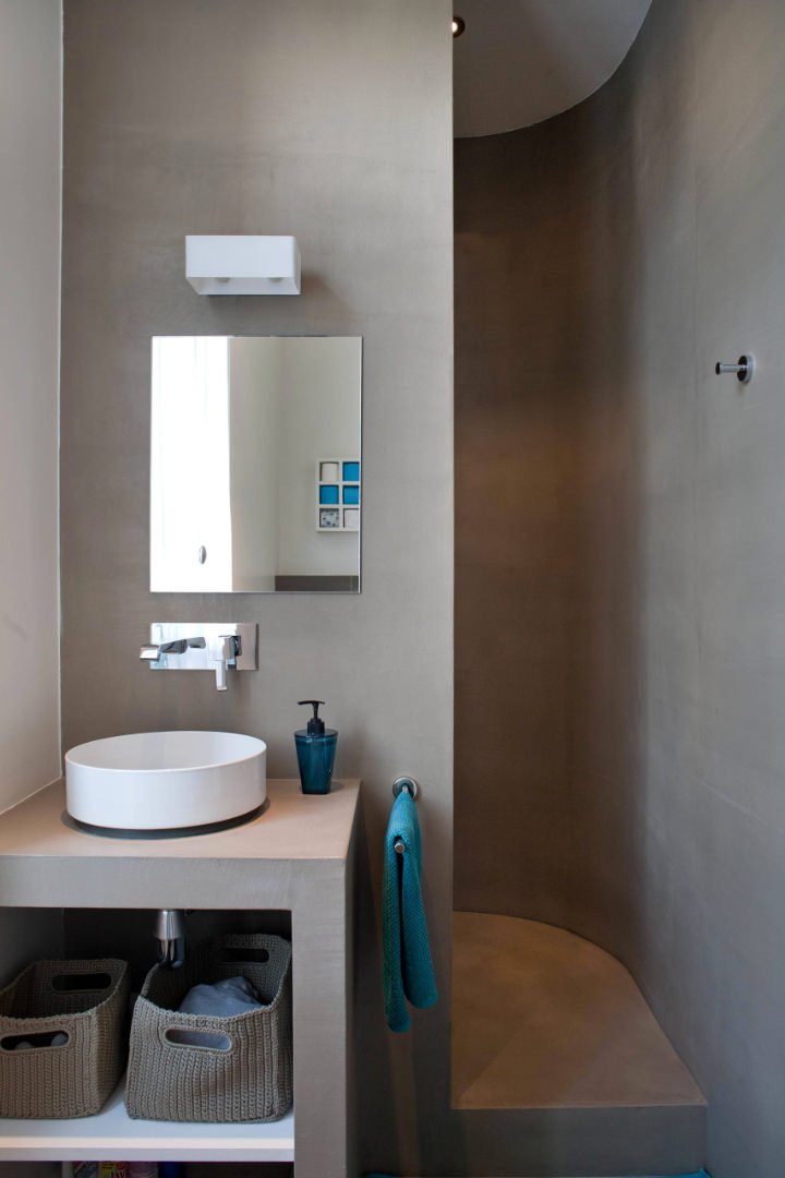 Idee per ristrutturare un piccolo bagno in muratura moderna: la doccia con la parete arrotondata è stata rivestita in resina, colore grigio cemento. Stile deciso e minimal, decisamente maschile.
