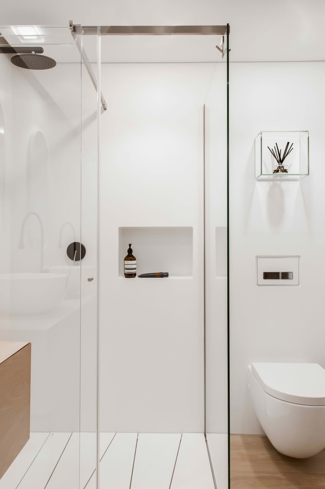 Modern minimal bathroom image with an almost imperceptible storage niche.  Simply plastered, white, with a slightly rounded edge.  Wooden floor and furniture, elements and details in tempered glass and stainless steel.