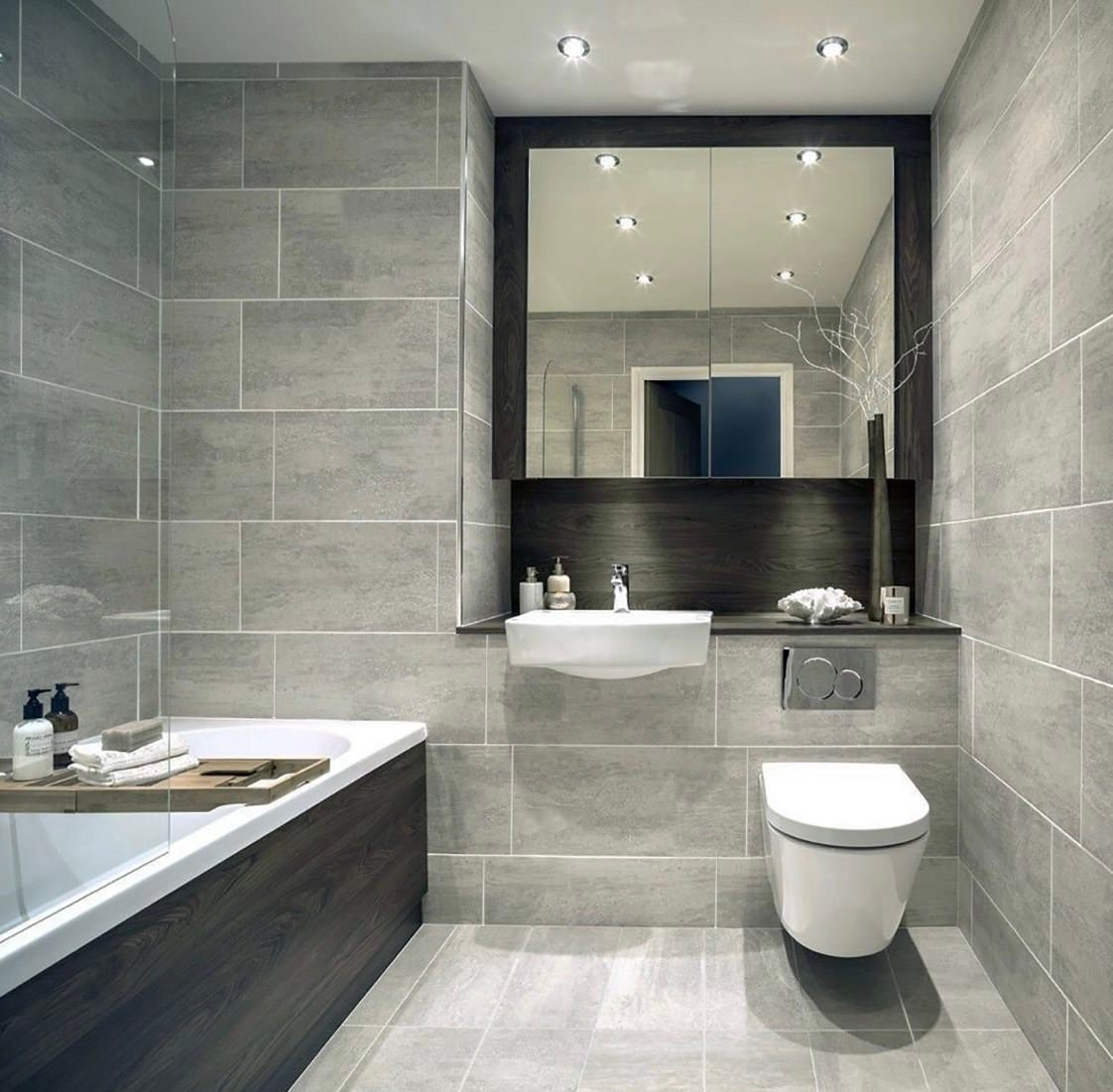 Small modern bathroom with gray porcelain floor and wall tiles up to the ceiling.  Over the cistern of the toilet and sink a recess has been created which houses a practical cabinet with mirror doors that widen the visual space.