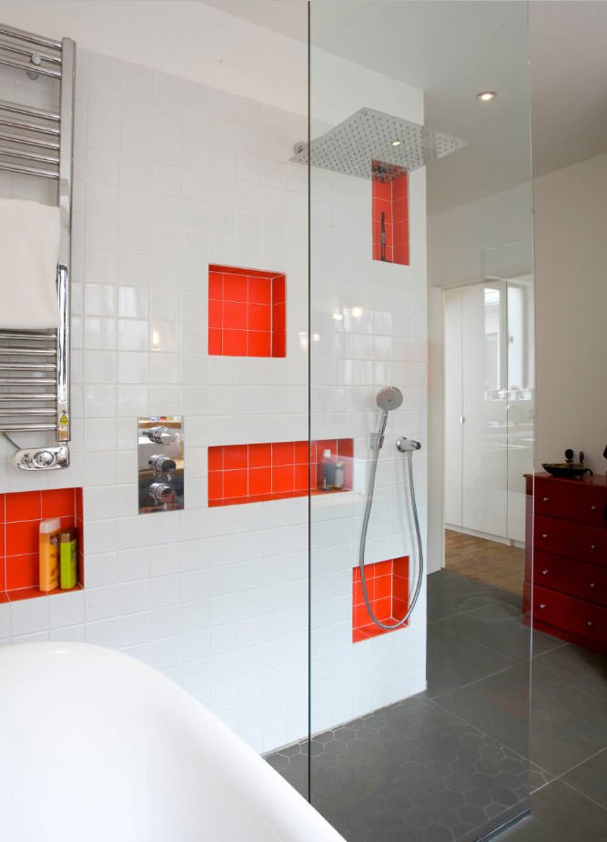 Idea bagno moderno, molto originale, con delle rientranze in piastrelle rosso arancione, in contrasto cromatico con le piastrelle bianche della parete. La doccia a filo pavimento presenta un'unica lastra di vetro temperato. Accenti in acciaio inox.