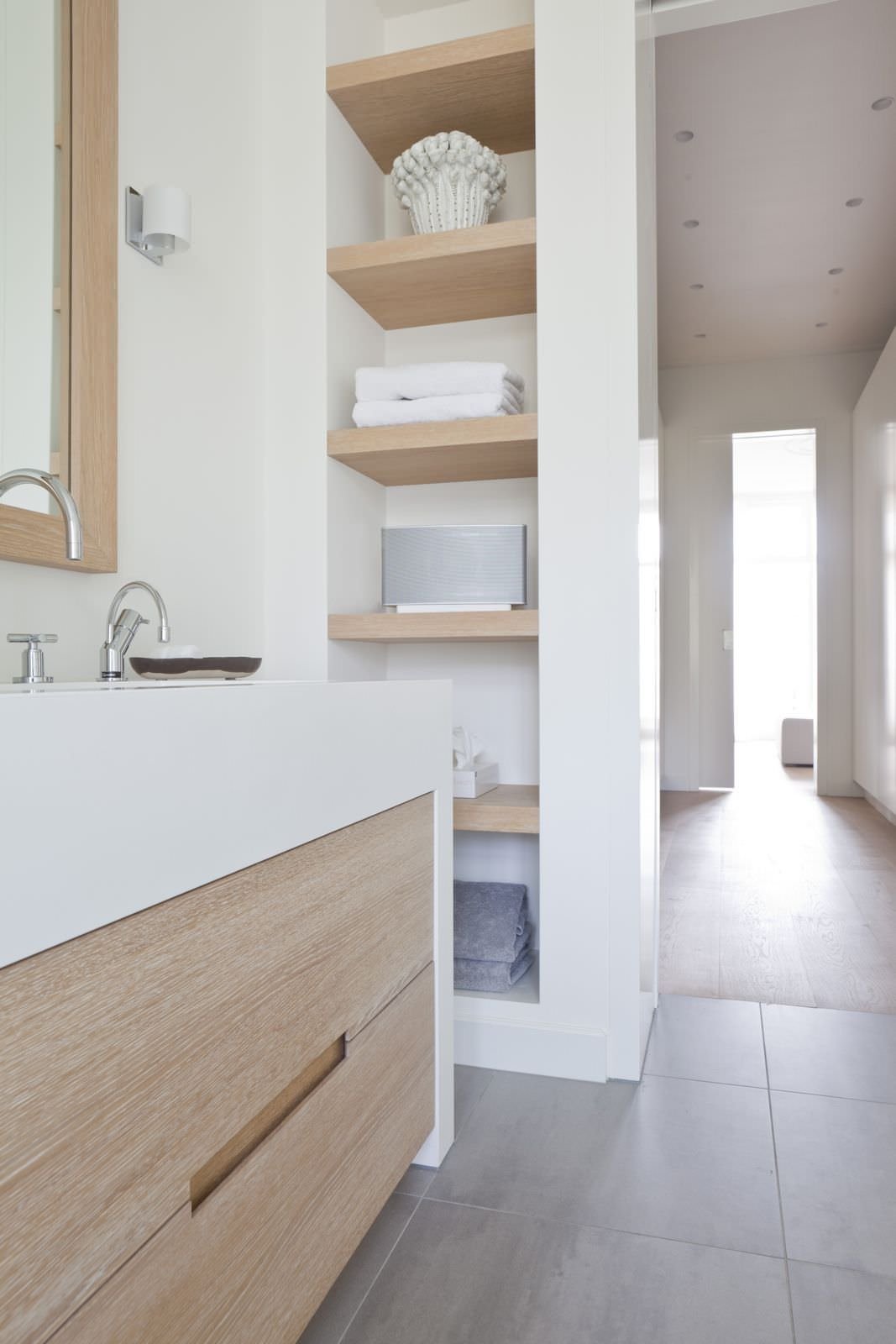 Modern bathroom design with masonry structure that becomes a large wardrobe with wooden shelves.  Warm colors of the earth, the white of the walls and the sink combines with the light wood and the stoneware floor, dove gray.  Beautiful idea.