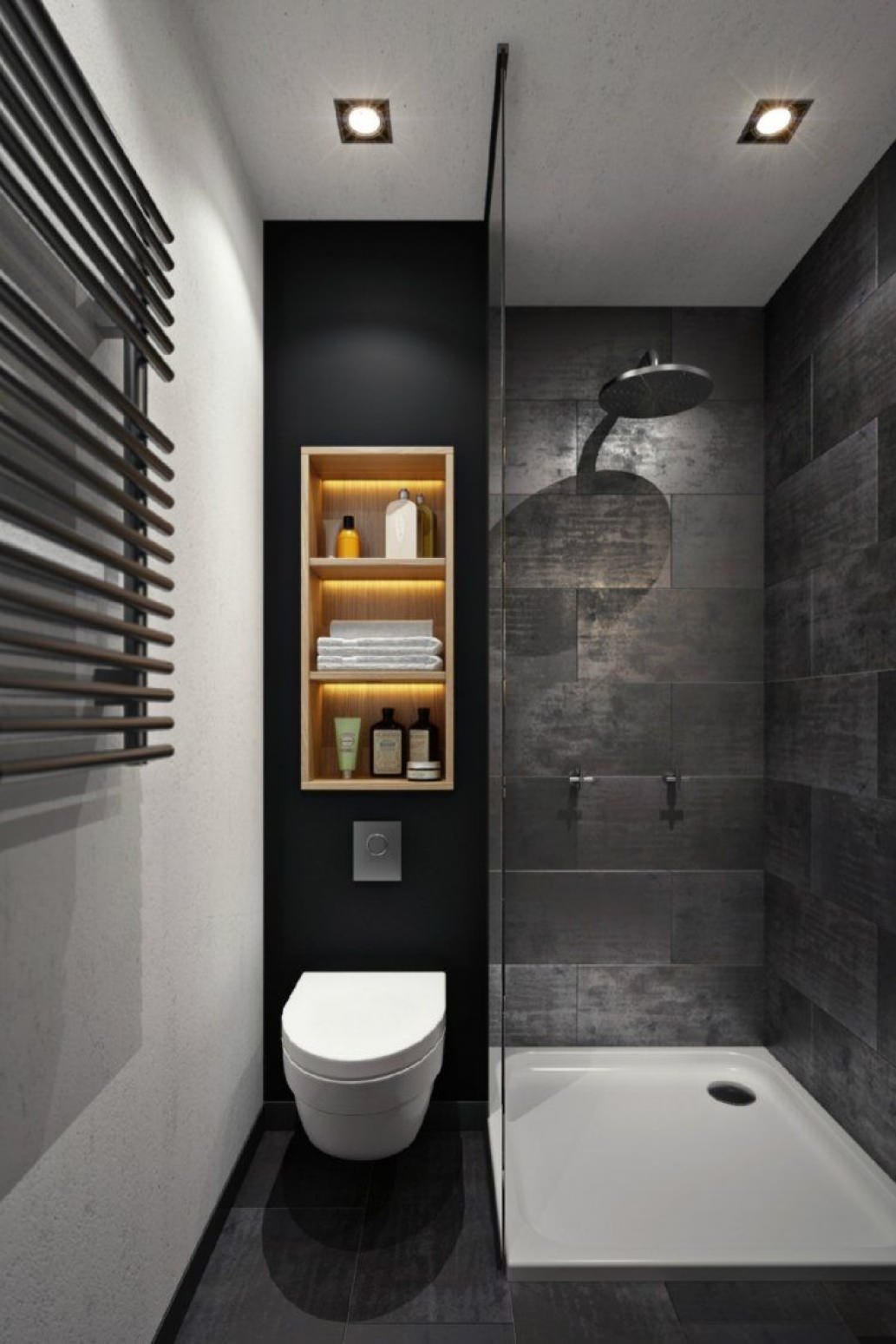 Piccolo bagno moderno nei colori bianco e nero con una nicchia sopra il wc creata in legno. Pavimento e rivestimento doccia in piastrelle di gres porcellanato grigio scuro con alcuni riflessi metallici. Controsoffitto con faretti da incasso.