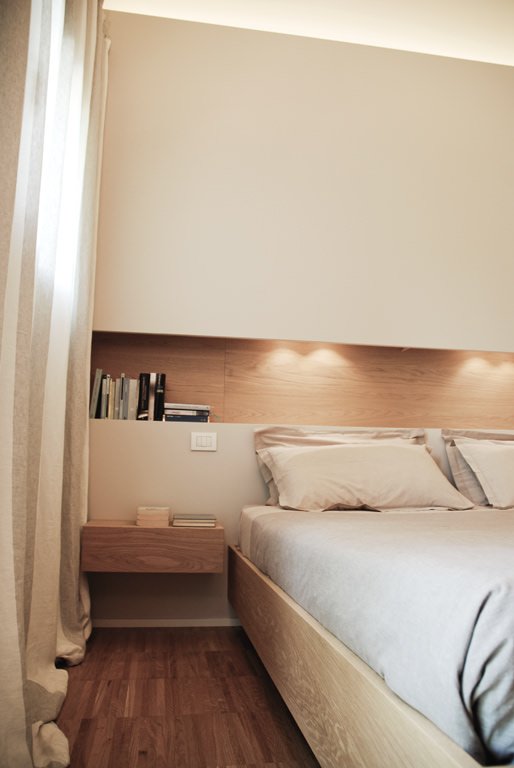 Modern bedroom with a niche above the headboard turned into a small bookcase.  LED diffused light on the ceiling - white walls - parquet floors -