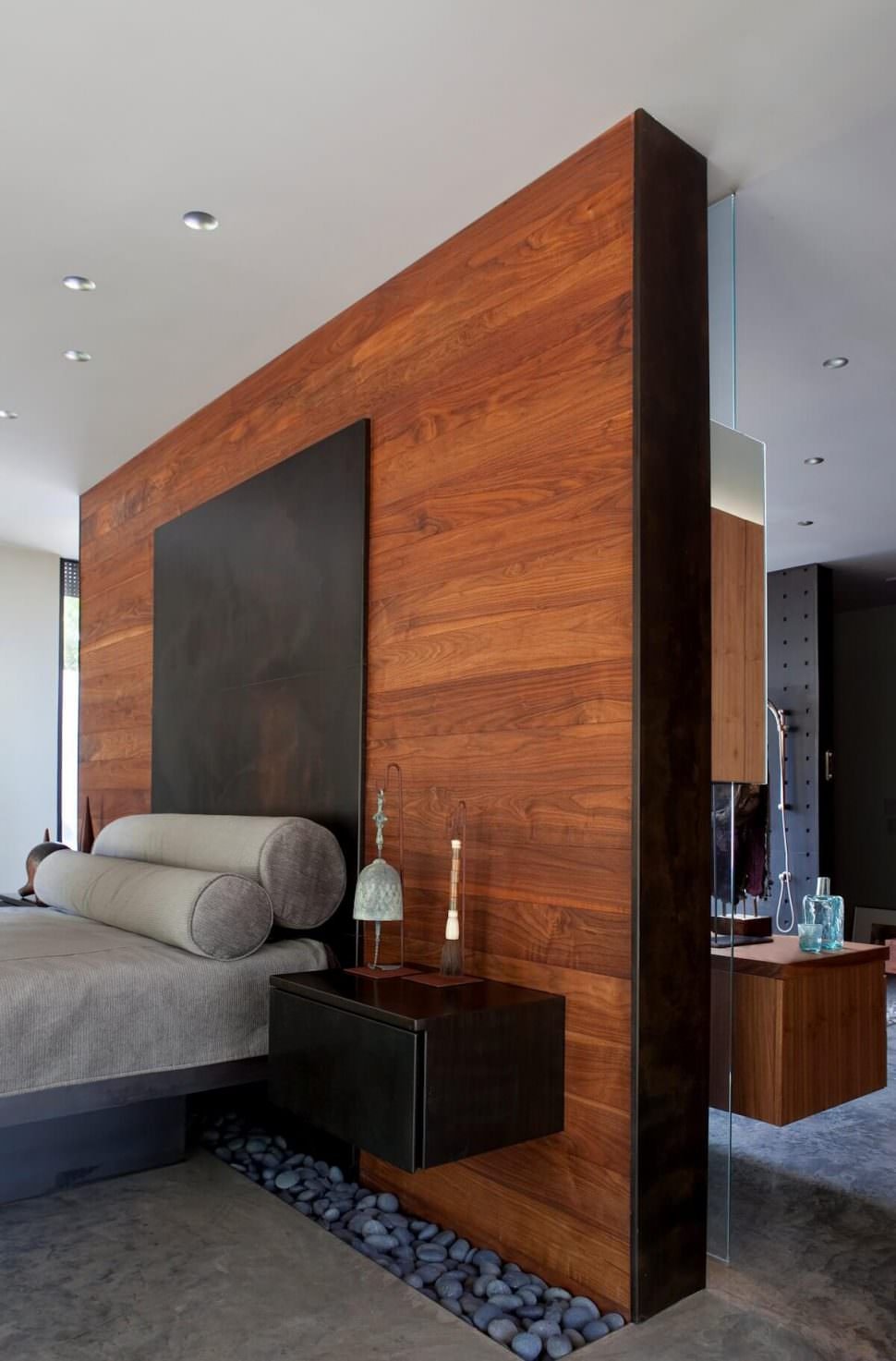 Very particular modern male bedroom with natural elements: wood used for the headboard wall, stones at the bottom of the same wall and iron used to create the headboard - concrete floor - gray color