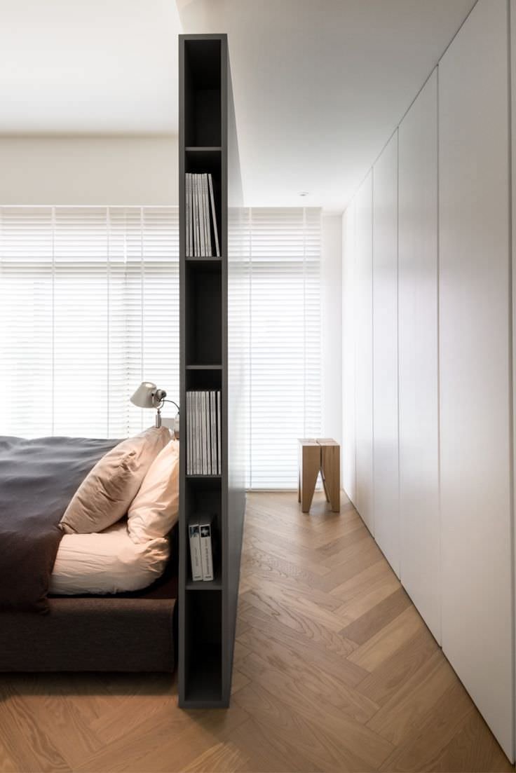 Modern bedroom with dividing wall between bed and wardrobes that acts as a small bookcase.  Modern, elegant and functional idea.  Wooden floor with herringbone pattern