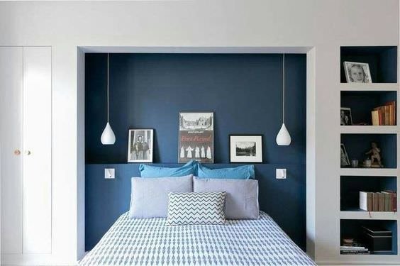 Modern bedroom with the headboard recessed into the wall in which the furnishings acquire the prominence of the framed objects.  The elegance of Prussian blue and the symmetry of hanging lamps stand out.