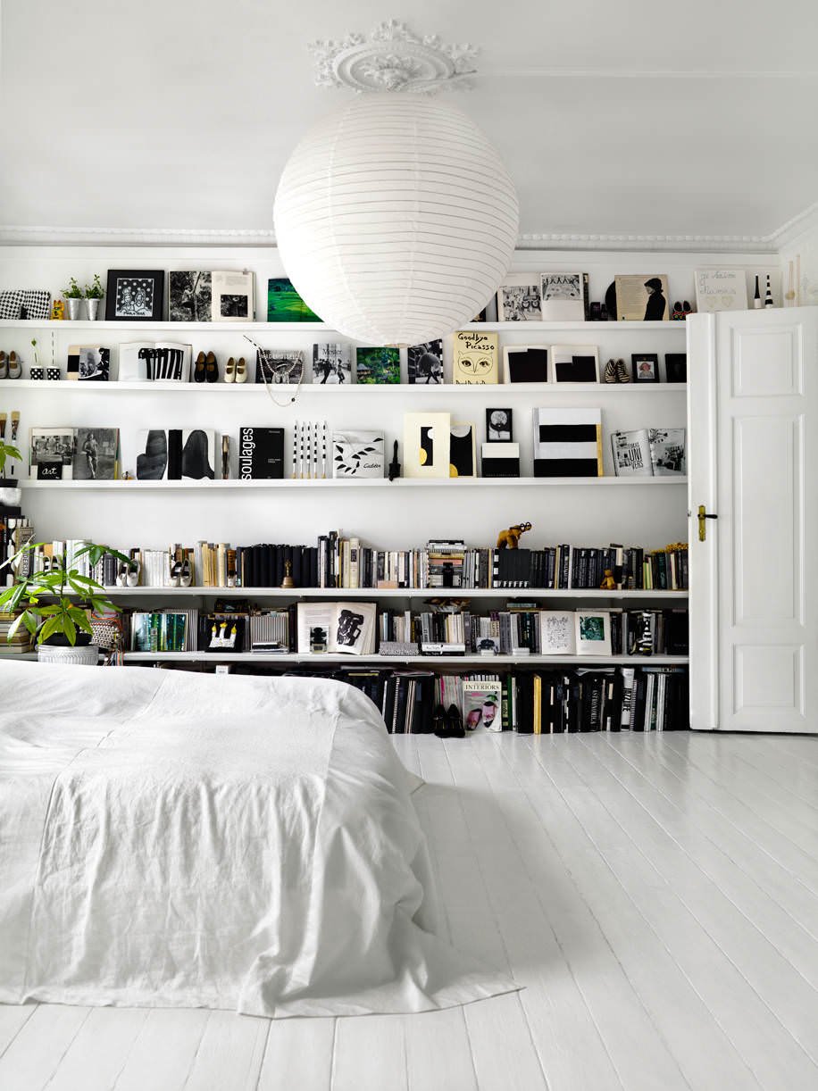 Beautiful total white bedroom in which the books in the bookcase on one wall add color to the room - white painted wooden floor