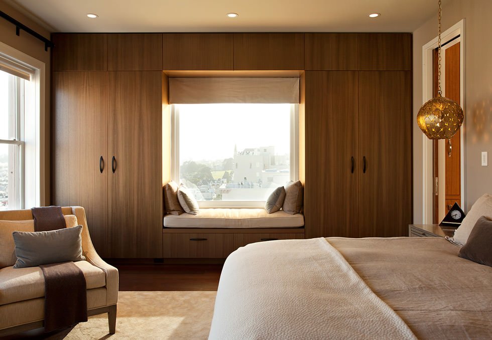 Camera da letto moderna e raffinata in cui l'armadio diventa la cornice di una finestra. Colori naturali: sfumature di marrone e bianco. Pavimento in legno e tappetto.