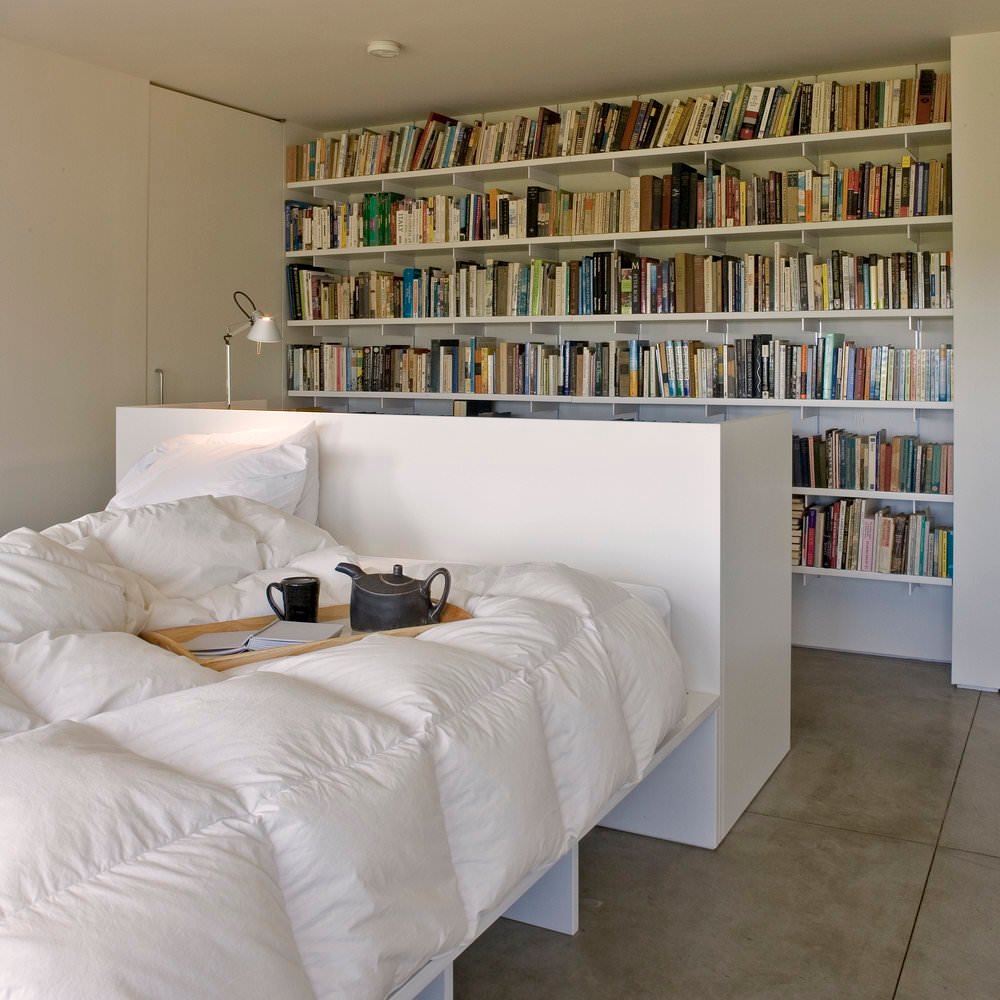 Minimal white bedroom with work station and bookcase that adds color and contrast.  Polished rough concrete floors