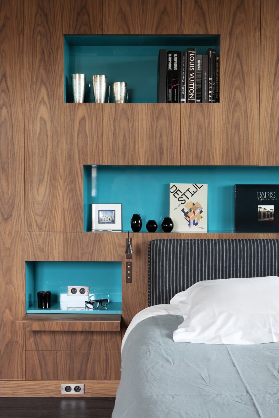 Modern bedroom with interesting headboard the whole wall covered in wood with various blue recesses