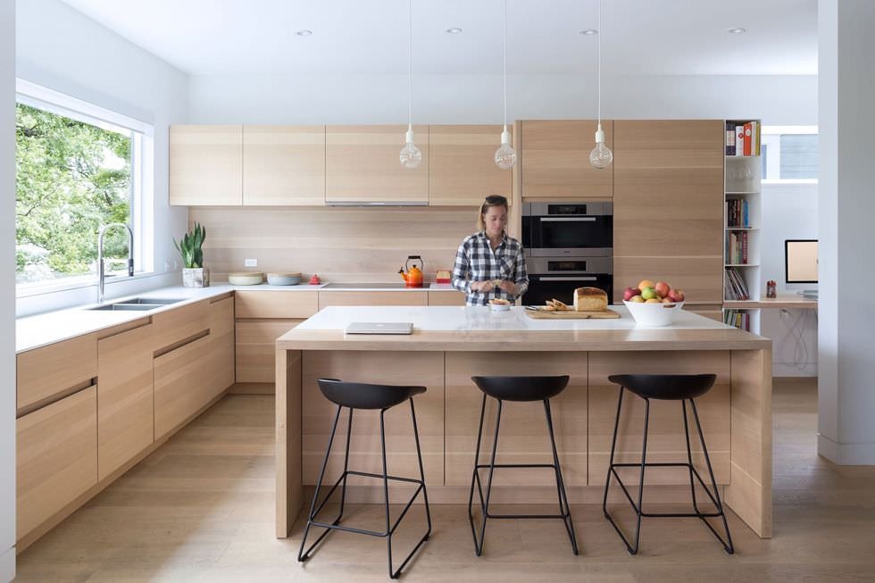 Immagine cucina con isola centrale realizzata in legno, materiale simile ai pavimenti. Top in acrilico bianco, sgabelli neri