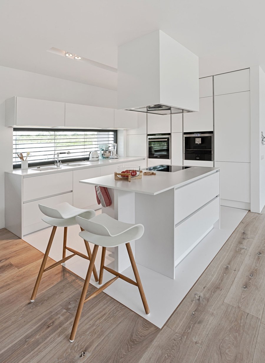 Bellissima cucina scandinava bianca con isola in un ambiente open space con delimitazione dello spazio attraverso il pavimento in pvc bianco. Idee cucine moderne ed eleganti.