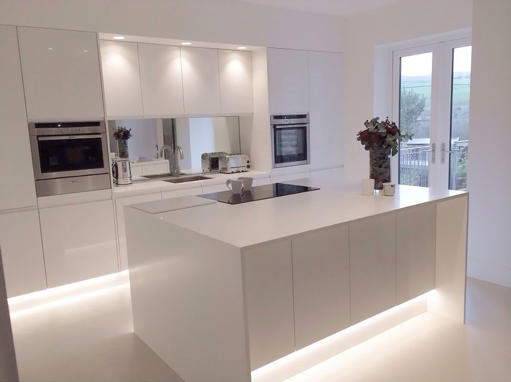 Immagine cucina moderna con isola bianca e stupenda illuminazione integrata nella parte inferiore dei mobili. Parette attrezzata a filo muro realizzata in laminato con top in corian.