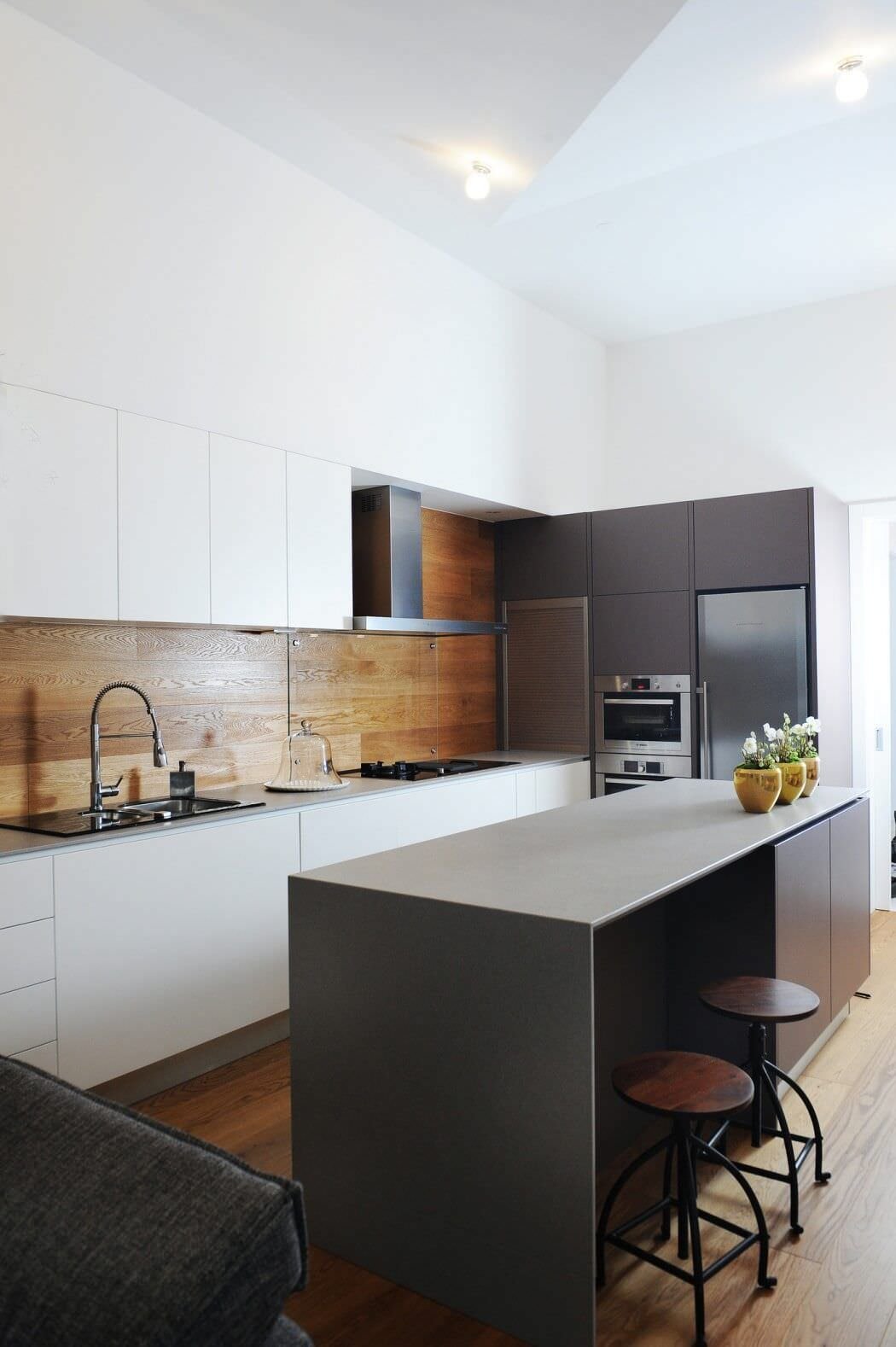 Immagine cucina stile minimal moderno con isola nera e mobili realizzata in laminato di colore bianco. Pensili filo muro e paraschizzi in teak.