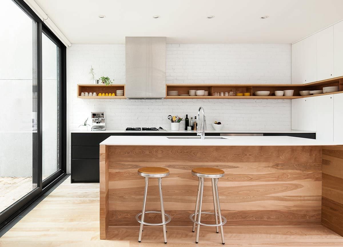 Esempio cucine moderne con isola centrale realizzata in legno. Top  bianco in acrilico ed i mobili disposti a parete di colore nero. Pensili aperti e muro in mattoni a vista verniciati.