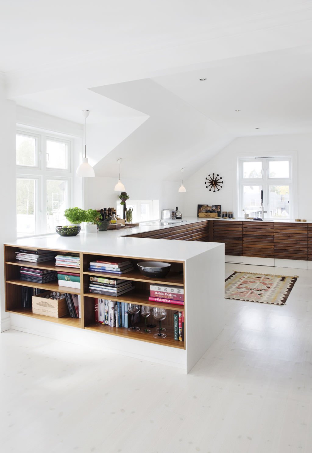 Stupenda idea di cucina moderna open space con mobili bassi in legno e bianco. In uno dei mobili è stata inserita una piccola libreria. Elegante, raffinato e funzionale.