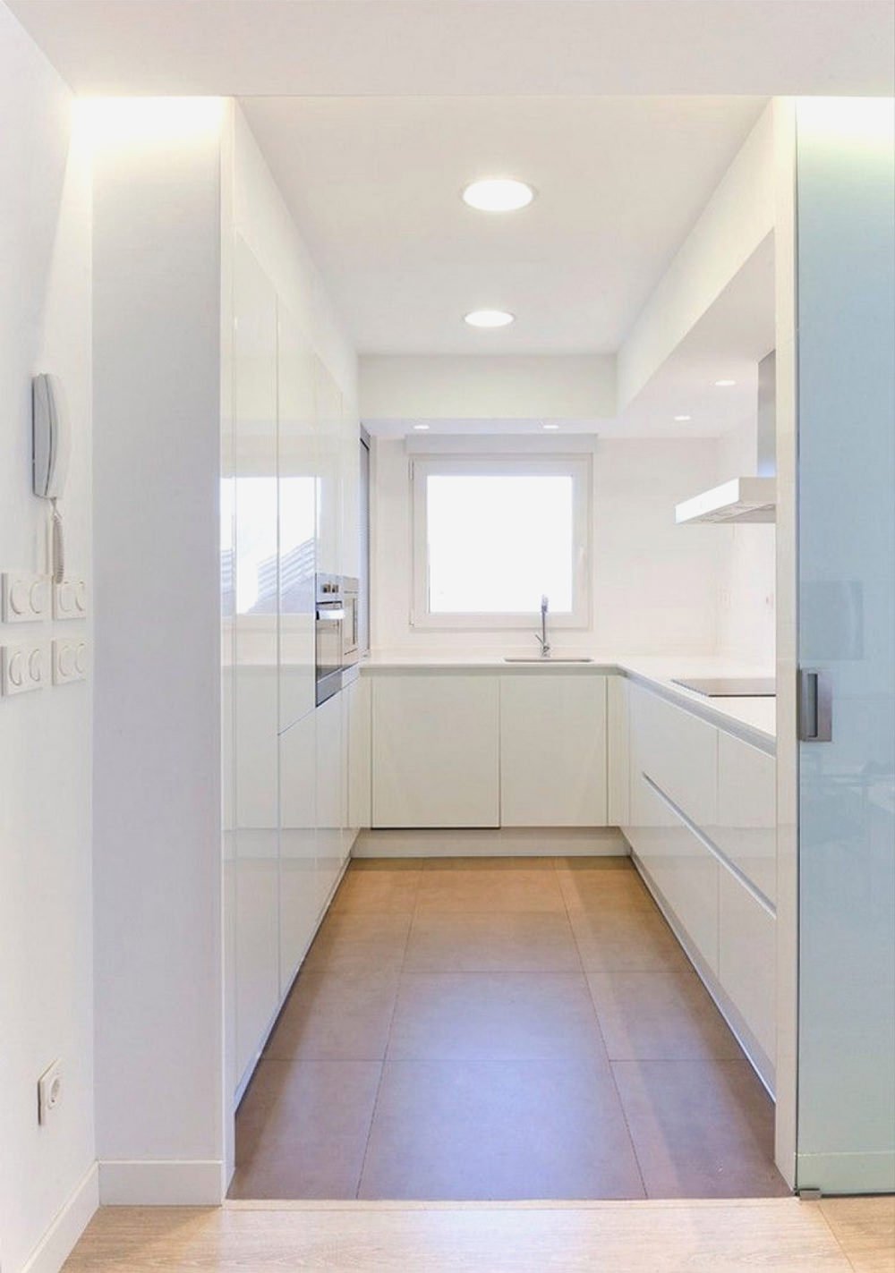 Piccola cucina bianca a U, con le ante laccate lucide, perfette per aumentare la luce e lo spazio visivo, così come la porta scorrevole in vetro. Pavimenti in gres. Idee cucina moderne bianche