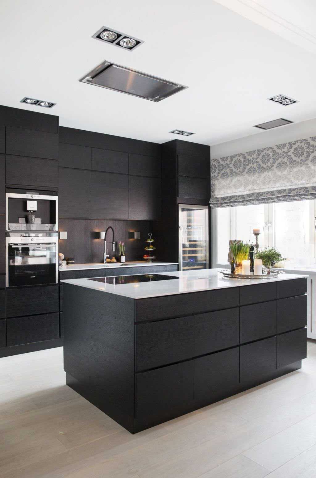 Immagine cucina moderna con isola, con contrasti di nero (mobili e ante) e bianco (il top). Cappa inserita nel soffitto in cartongesso, così come il sistema di illuminazione.