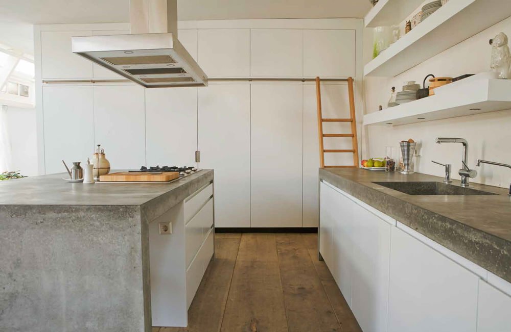 Idea cucina moderna con isola, top in cemento, mobili e mensole in laminato bianco. Pavimenti in legno.