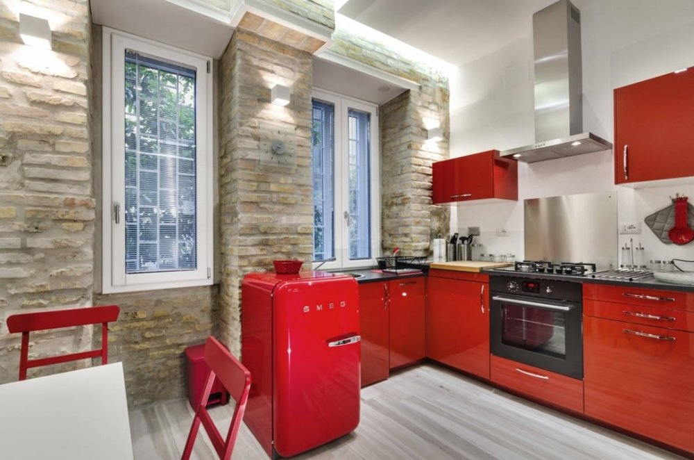 Cucina piccola, stile moderno, con i mobili in laccato rosso. Muri in mattoni a vista. Pavimenti in marmo. Particolare illuminazione con gole di luce inserite nel controsoffitto in cartongesso.