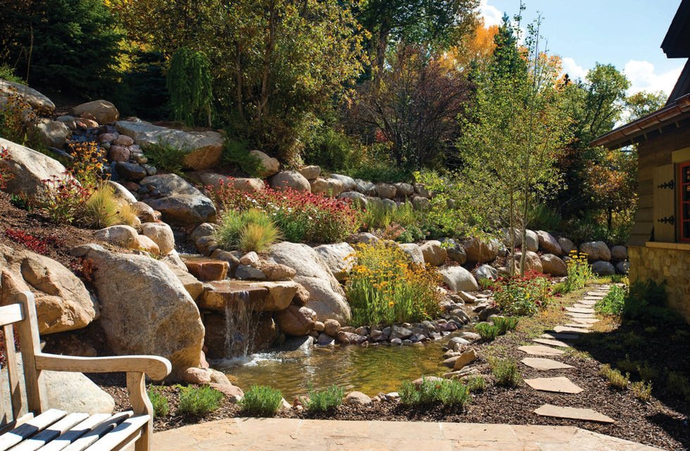 Incantevole giardino roccioso di aspetto molto naturale con pietre, alberi, piante, fiori e una piccola cascata d'acqua