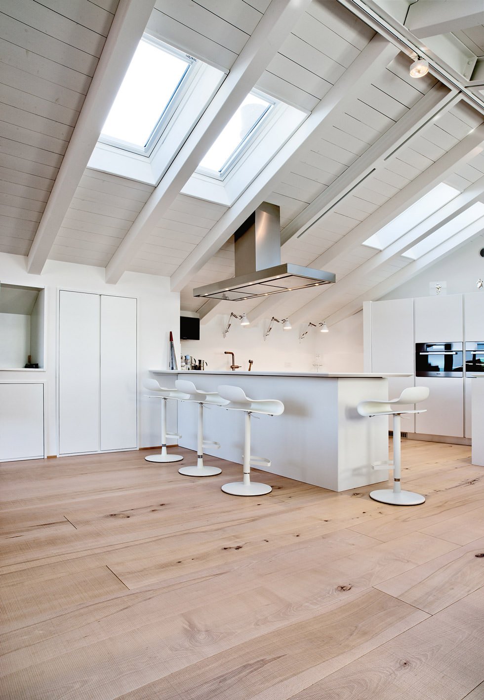 Idee per mansarde moderne ben illuminate - cucina open space con pareti, soffitti, arredi e mobili bianchi e pavimenti in legno chiaro per un ulteriore luminosità
