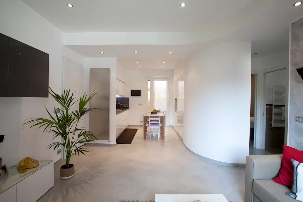 Zona living con interessanti forme e movimenti delle pareti e del controsoffitto. Ambiente molto luminoso con pavimento chiaro, pareti bianche e controsoffitto con illuminazione a led
