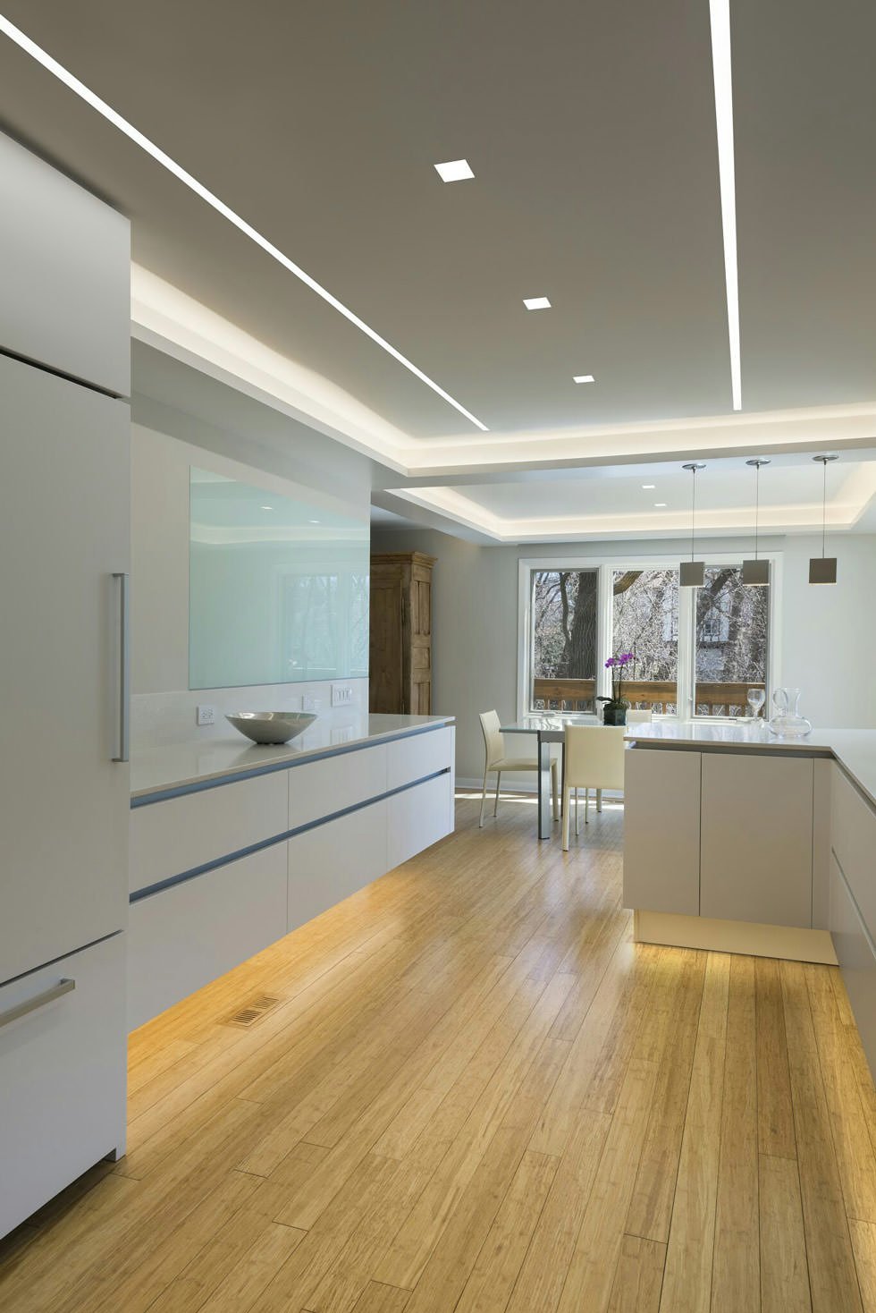 Elegante cucina moderna in bianco e grigio con un ottimo sistema di illuminazione - sul soffitto con gole luminose e sotto i mobili