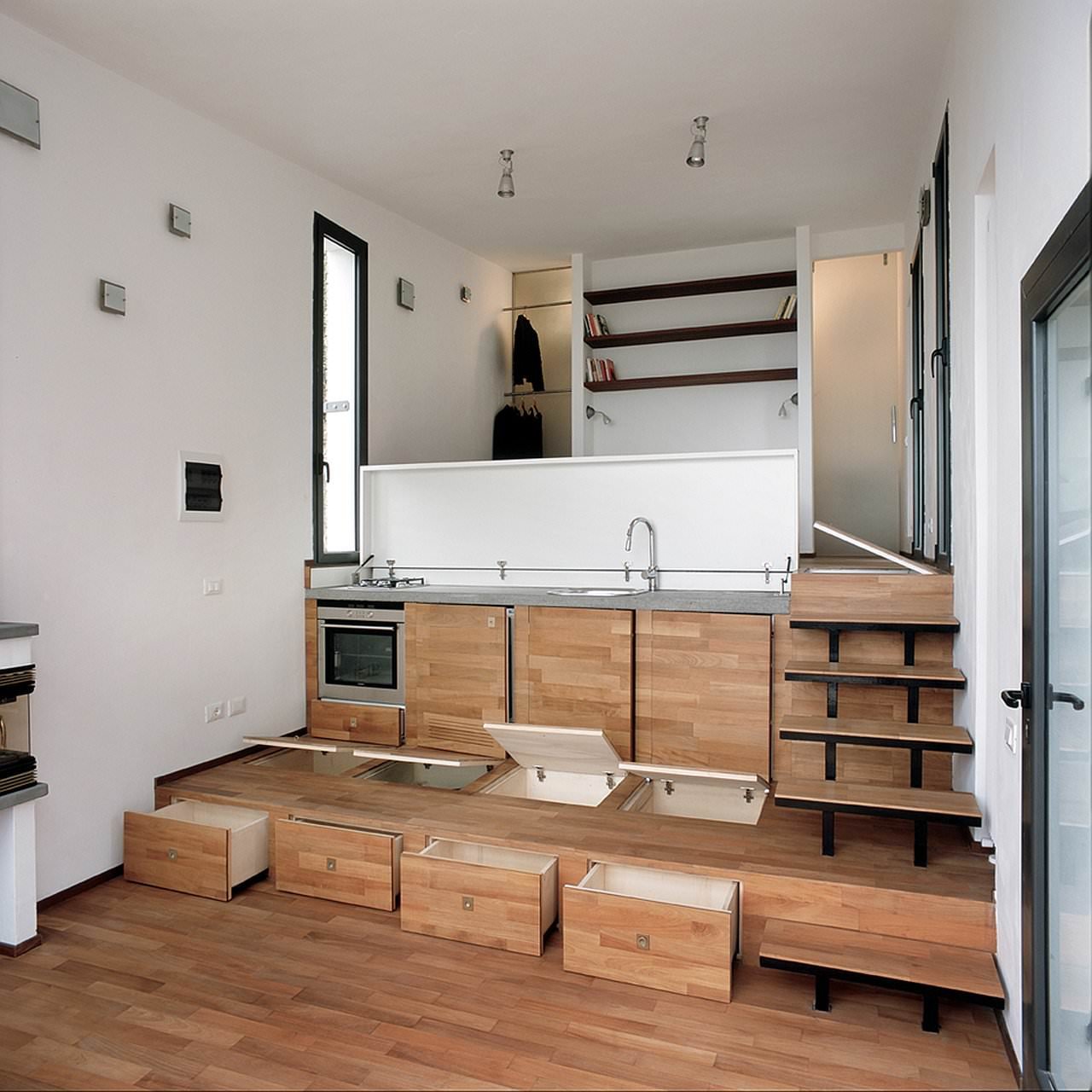 Interno casa cucina, con il pavimento che si trasforma in un contenitore di oggetti per razionalizzare il piccolo spazio a disposizione