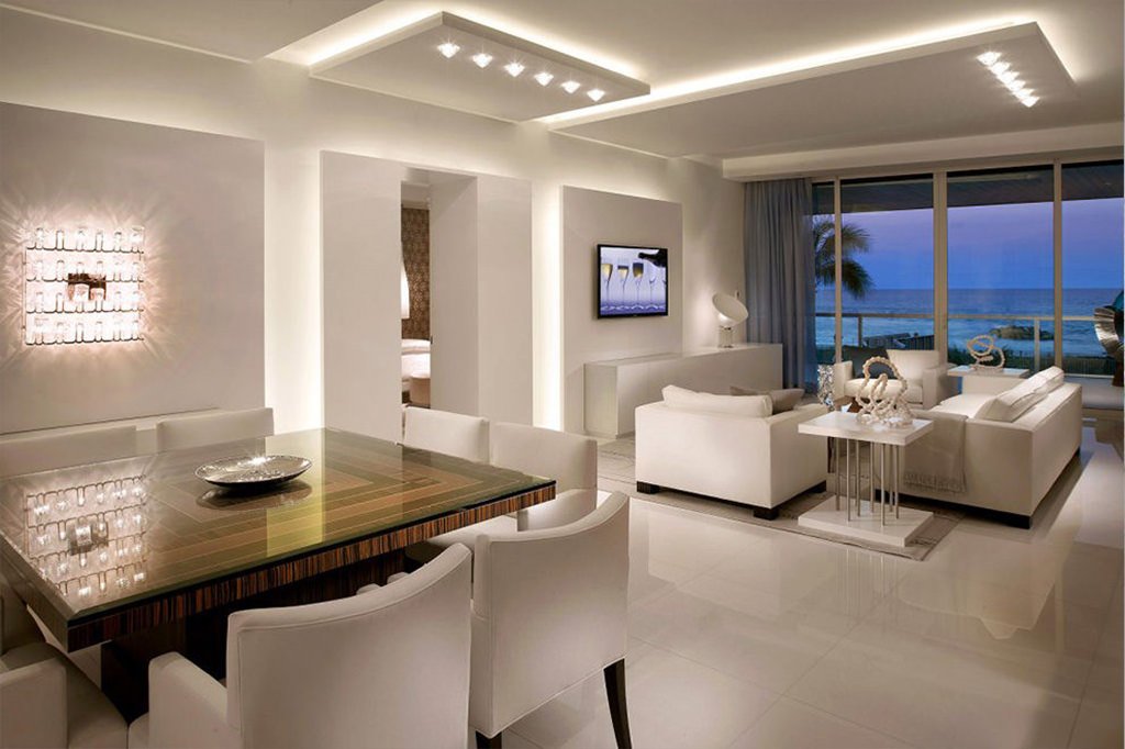 Ambiente open space moderno e molto luminoso con soggiorno e sala da pranzo - varie strutture in cartongesso presenti sui muri e sul soffitto per un effetto originale e scenografico - arredamento bianco abbinato al legno - guida completa costo elettricista - preventivo elettricisti