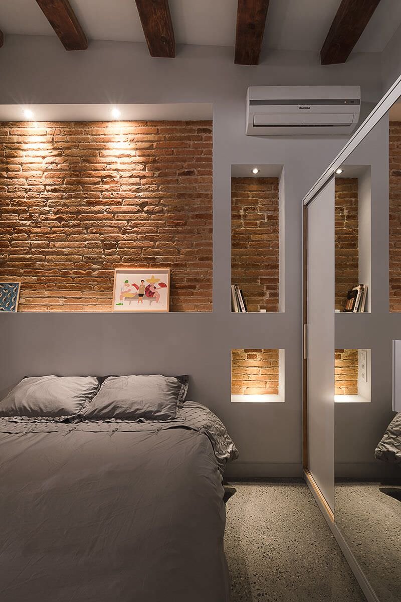 Moderna camera da letto con nicchie in cartongesso realizzate sopra un muro con mattoni a vista per un effetto visivo di grande impatto. La luce dei faretti illumina la parete mettendola in evidenza.