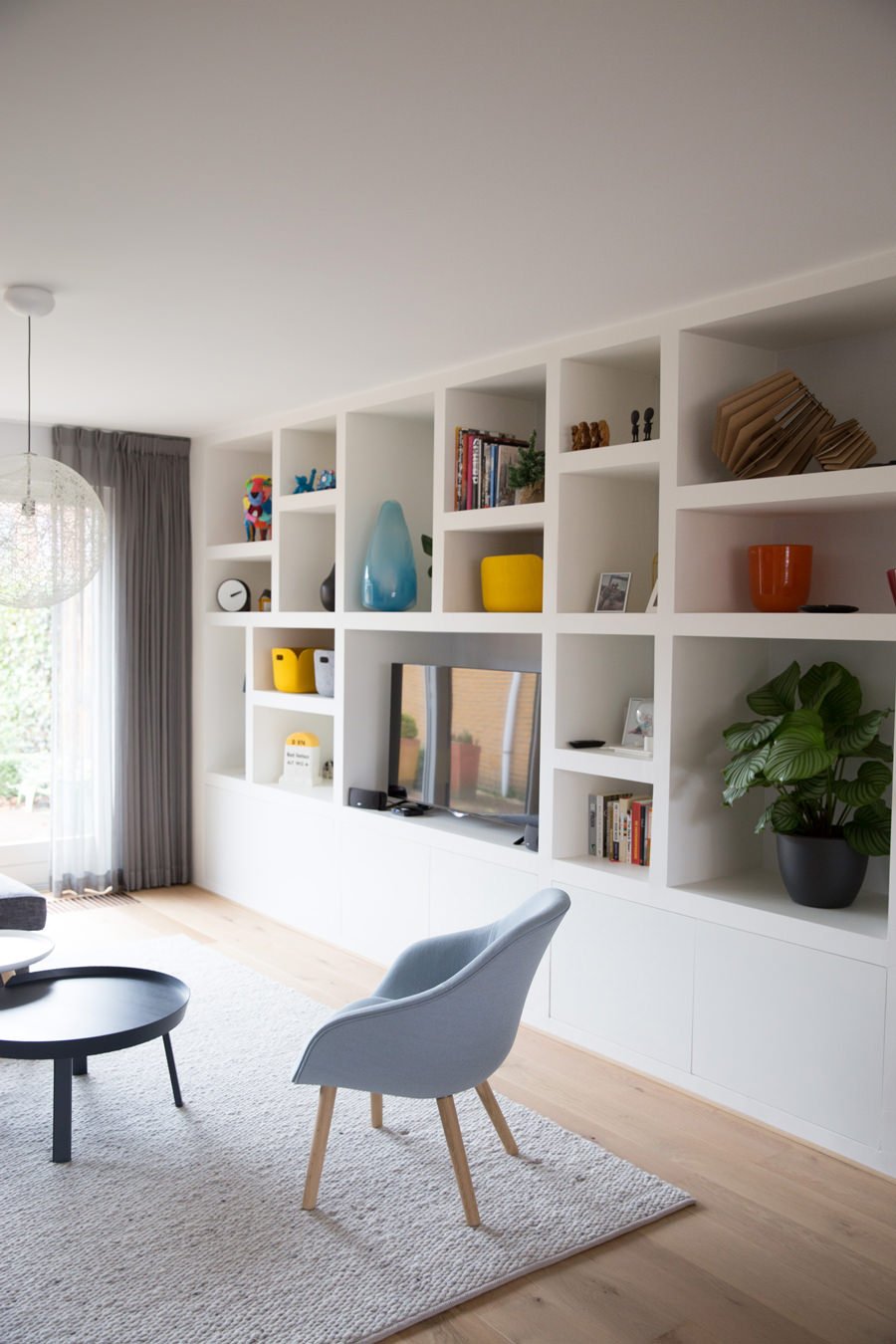 Salotto scandinavo moderno con parete attrezzata che ospita decorazioni dai colori vivaci. Nella parte inferiore presenta ante a filomuro. Articolo idee e prezzi pareti attrezzate in cartongesso