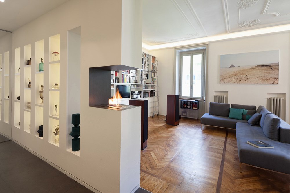 Stupenda parete attrezzata in cartongesso per dividere lo spazio living. Divisorio trasparente con nicchie a diversa altezza. Un piccolo caminetto a bioetanolo inserito nella struttura valorizza l'ambiente. Velette con luce diffusa e decorazioni in gesso sul soffitto