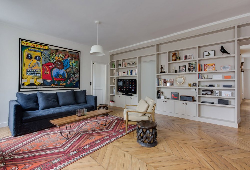 Soggiorno contemporaneo eclettico che abbina vari stili. Parete libreria in cartongesso verniciata in grigio tortora, pavimenti in legno a spina di pesce.