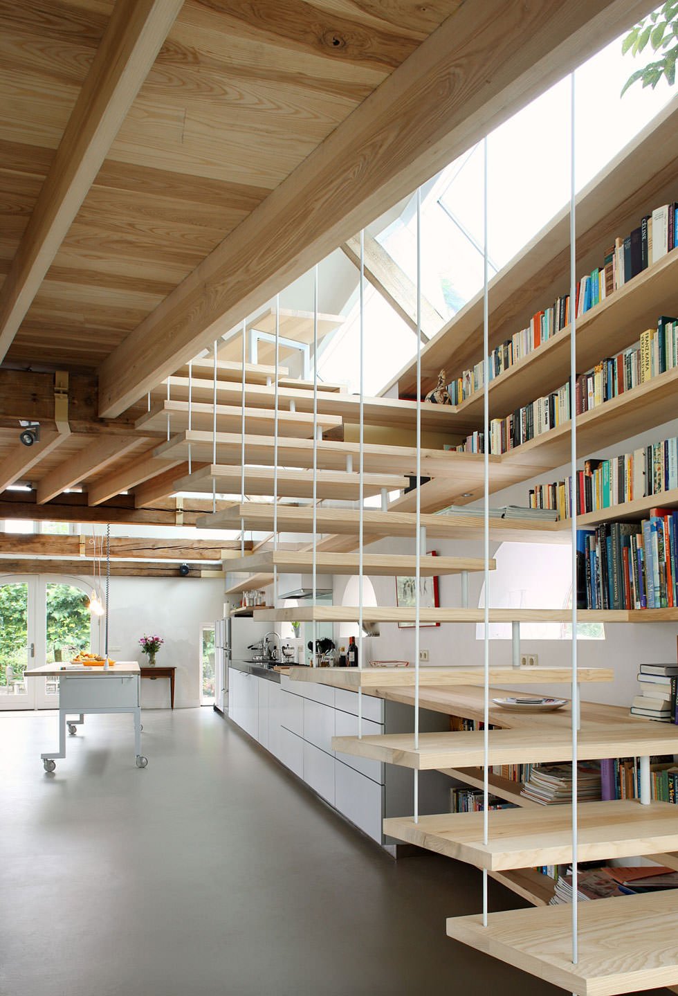 Immagine scala moderna in legno che si trasforma in un allestimento unico, diventando parte degli scaffali della libreria ma anche del top della cucina