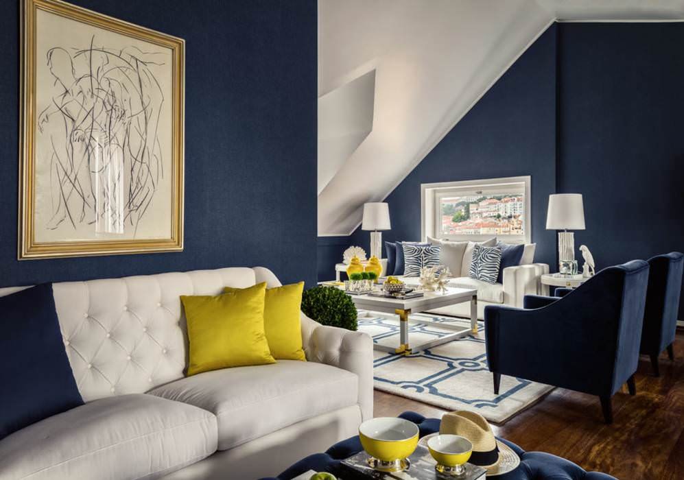 Piccolo soggiorno nella mansarda con i pareti blu scuro. Stile di lusso con vari elementi dorati e decori color giallo sole