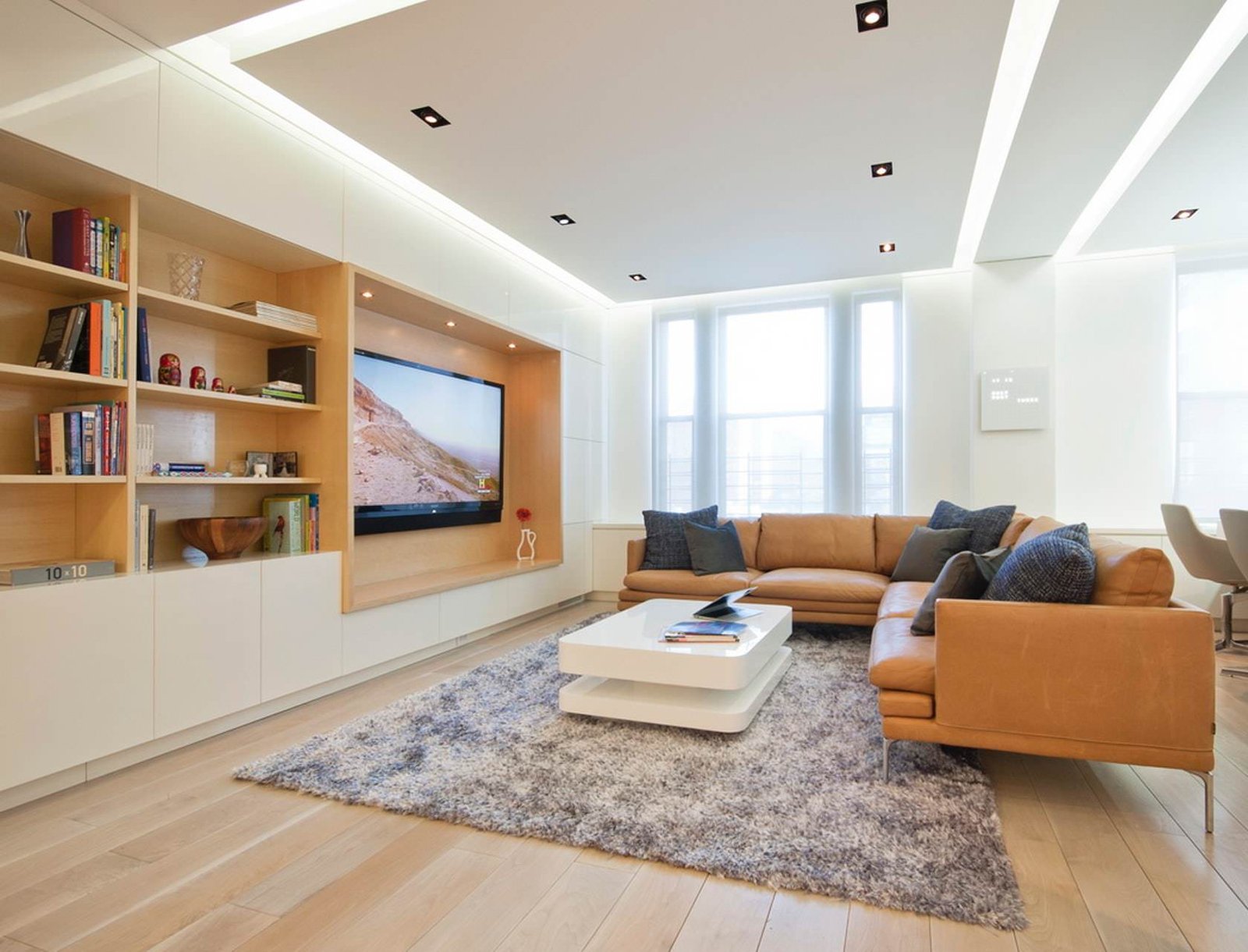 Idea soggiorno moderno in colori dominanti bianco e marrone. Pavimento in legno così come l'interno della libreria. Soffitto in cartongesso con particolare illuminazione
