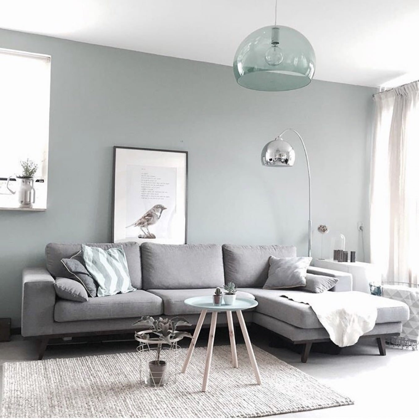 Bellissimo salotto stile nordico con contrasto delicato tra divano a L in tessuto grigio e parete grigio tè verde - pavimento in cemento