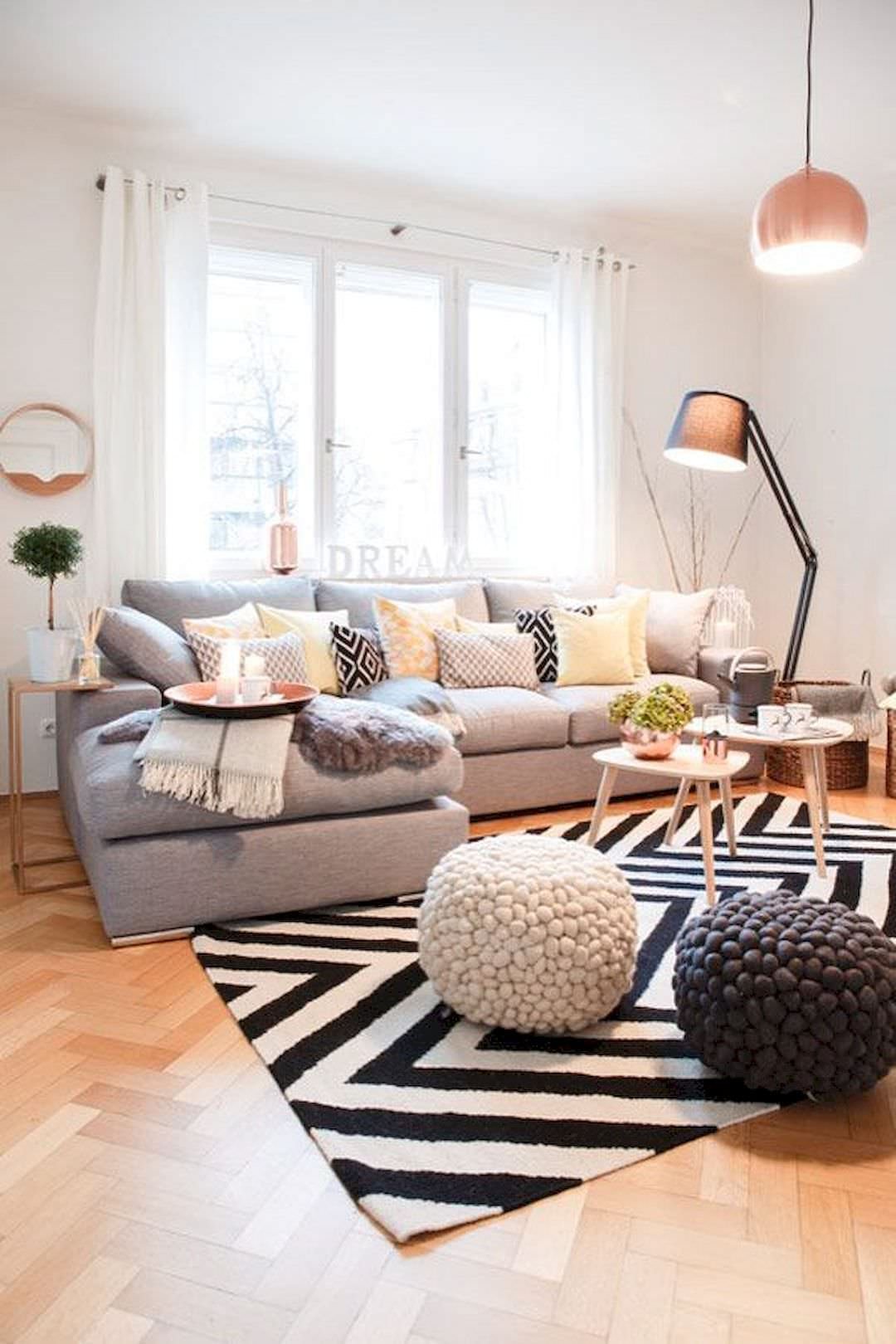Piccolo salotto scandinavo luminoso ed accogliente, con vari giochi di prospettiva per ampliare lo spazio visivo: tappeto a righe, i piccoli tavolini rotondi da caffè, il divano posizionato vicino alla finestra ed anche la alta lampada.