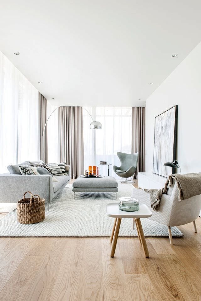 Salotto scandinavo moderno molto luminoso, con finestre fino al soffitto. Caldo ed accogliente, in tonalità di grigio con pavimento ed alcuni elementi in legno. Lampada da terra ad arco. Design minimal, elegante ed essenziale.