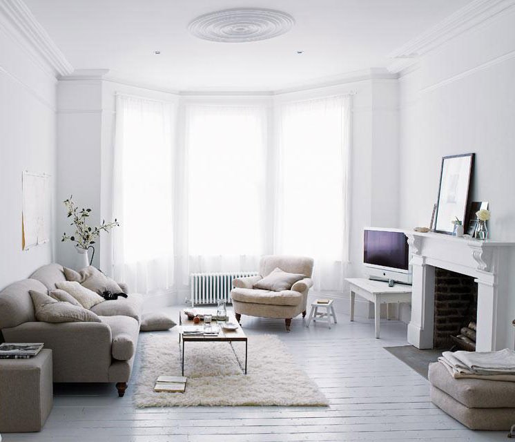 La grande finestra centrale riempie di luce questo salotto stile scandinavo shabby, con il pavimento in legno verniciato in bianco, come la cornice del camino. Divano grigio tortora in stoffa.