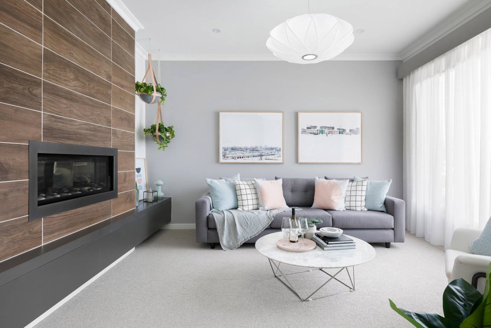 Immagine salotto moderno scandinavo, con camino a bioetanolo disposto su una parete rivestita in lunghe lastre di gres porcellanato, effetto legno. Nella stanza domina il grigio (divano e colore pareti) ed alcuni tocchi di colore pastello.