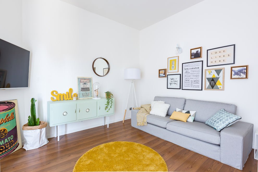 Piccolo living stile nordico, allegro ed elegante, con pavimento in legno, divano in stoffa grigio e vari tocchi di colore tra giallo, verde e blu. Moderno ed accogliente.