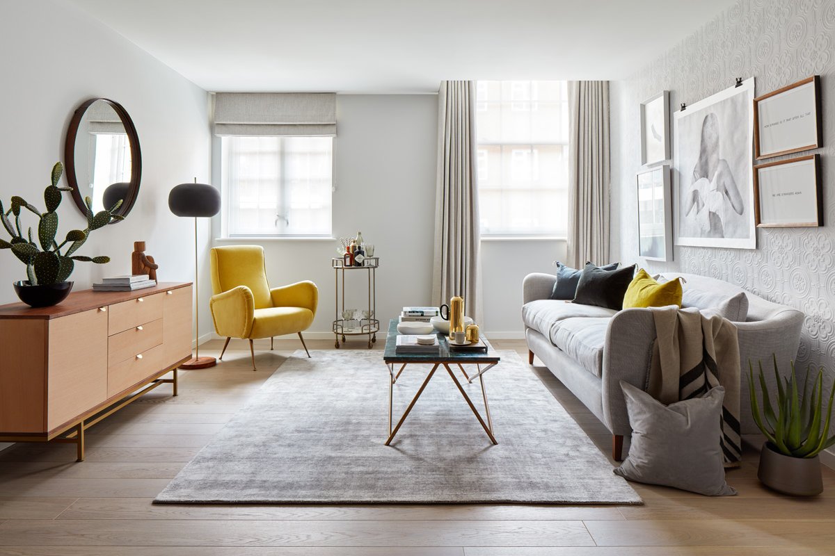 Un altro soggiorno scandinavo, elegante e raffinato, in cui dominano il colore grigio (pareti, divano in stoffa e tappeto), il legno (pavimento, mobile e le cornici dei quadri), alcuni tocchi di giallo (poltrona e cuscini) ed il verde naturale delle piante.