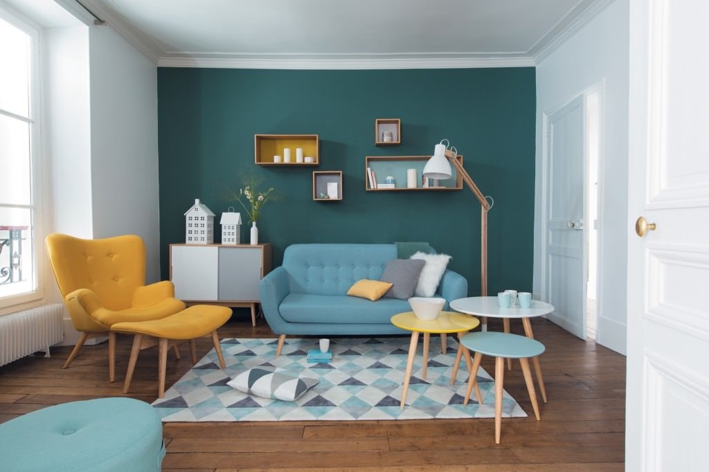 Immagine soggiorno moderno scandinavo con parete d'accento in blu cadetto, colore che ridimensiona i complementi d'arredo, esaltando il divano blu chiaro e la poltrona gialla. Molto interessante questo abbinamento di colori freddi e caldi.