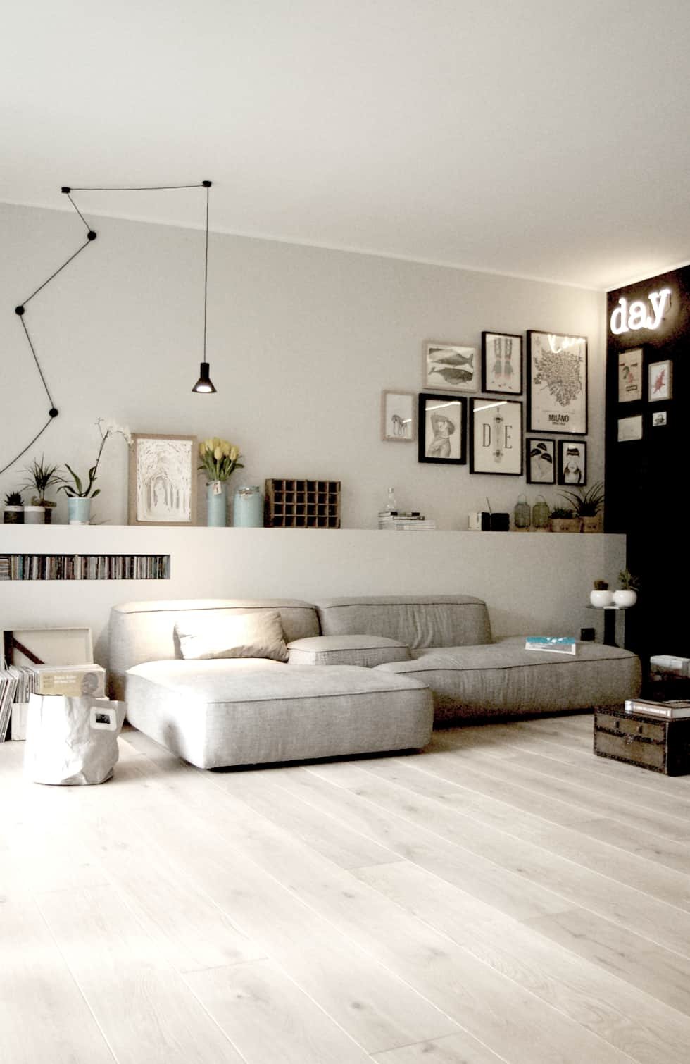 Stupendo soggiorno scandinavo che denota modernità ed eleganza con grande divano in tessuto grigio chiaro, parquet in rovere ed una parete d'accento in nero. Molto interessante la testata del divano creata in muratura, usata come base d'appoggio e che ospita una nicchia per i libri
